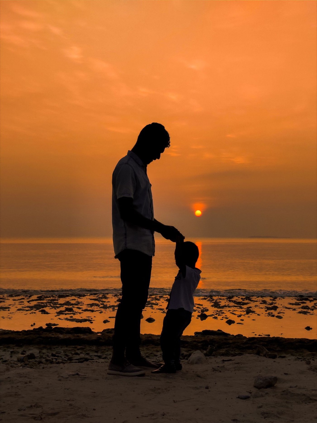A parent and child holding hands, silhouetted against a golden sunset